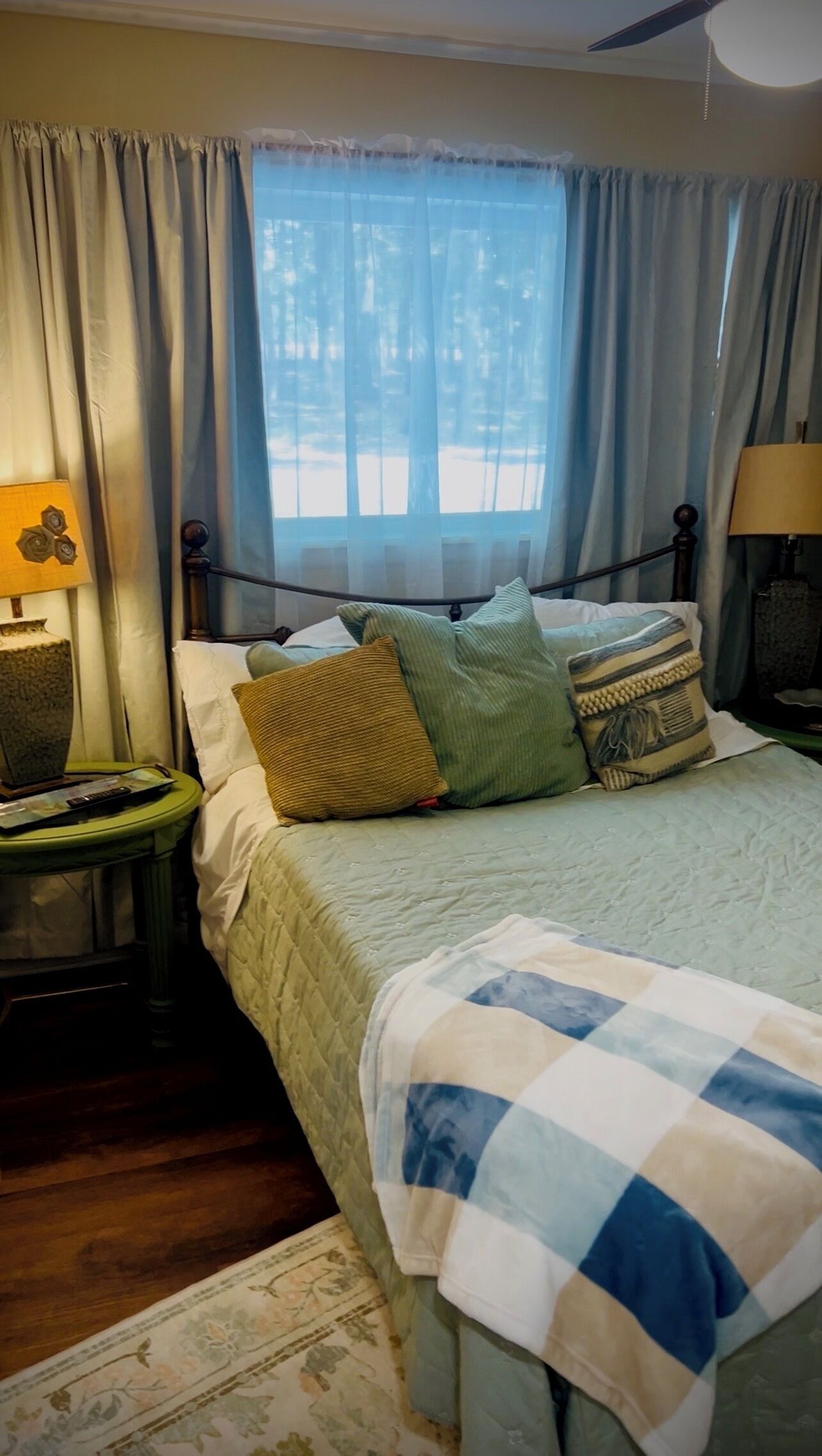 A bedroom with a bed, pillows, a nightstand, a lamp, and a window with curtains.