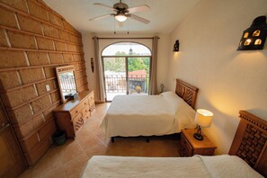 A bedroom with two beds, a ceiling fan, a window with a view of greenery, and a brick wall. - Casa Melmar Pool & Garden in Cuernavaca (Tres de Mayo)