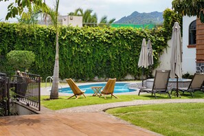 A pool area with lounge chairs and umbrellas, surrounded by a hedge and a view of hills. - Casa Melmar Pool & Garden in Cuernavaca (Tres de Mayo)