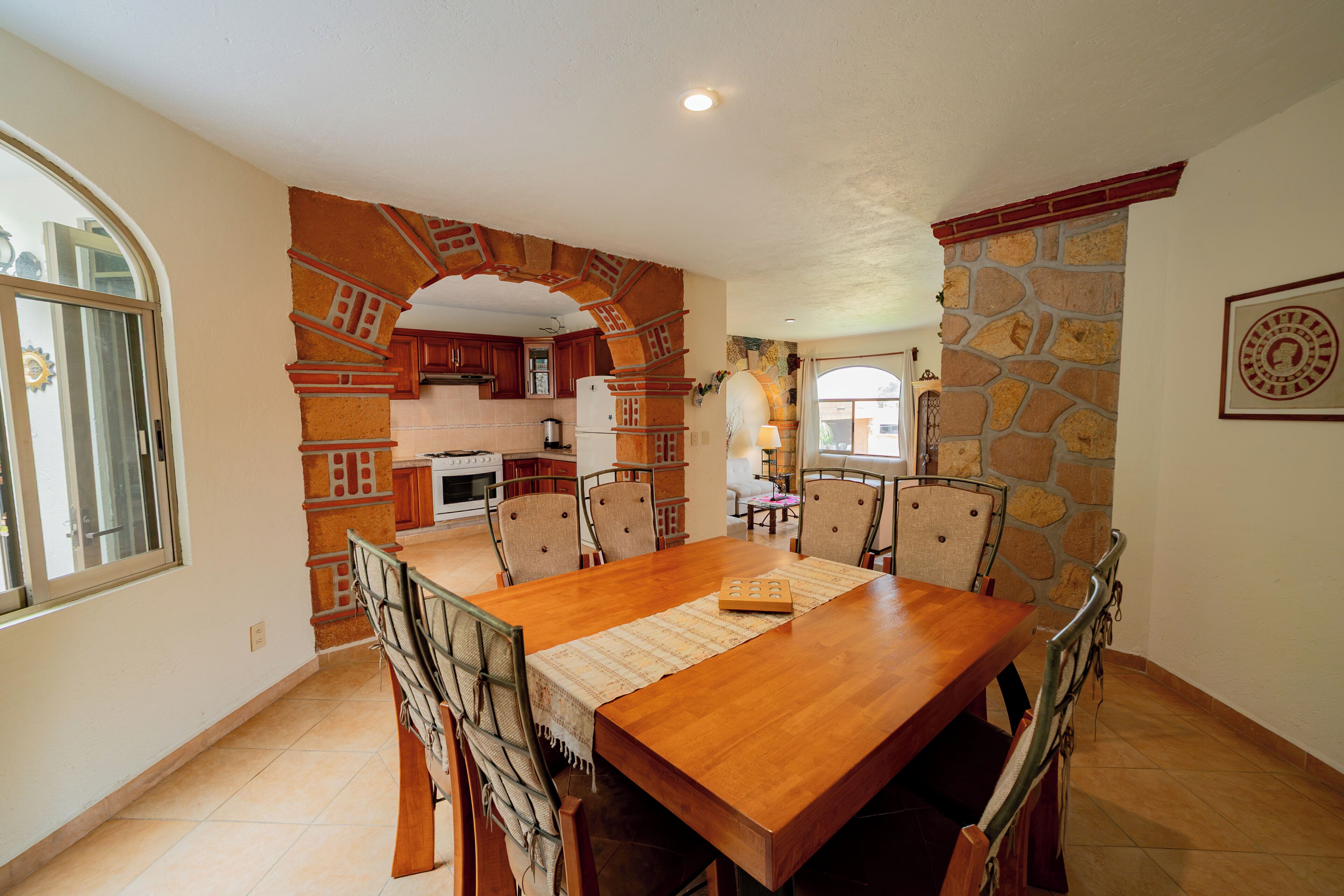 Un comedor con una mesa y sillas de madera, una cocina al fondo y una pared de piedra.