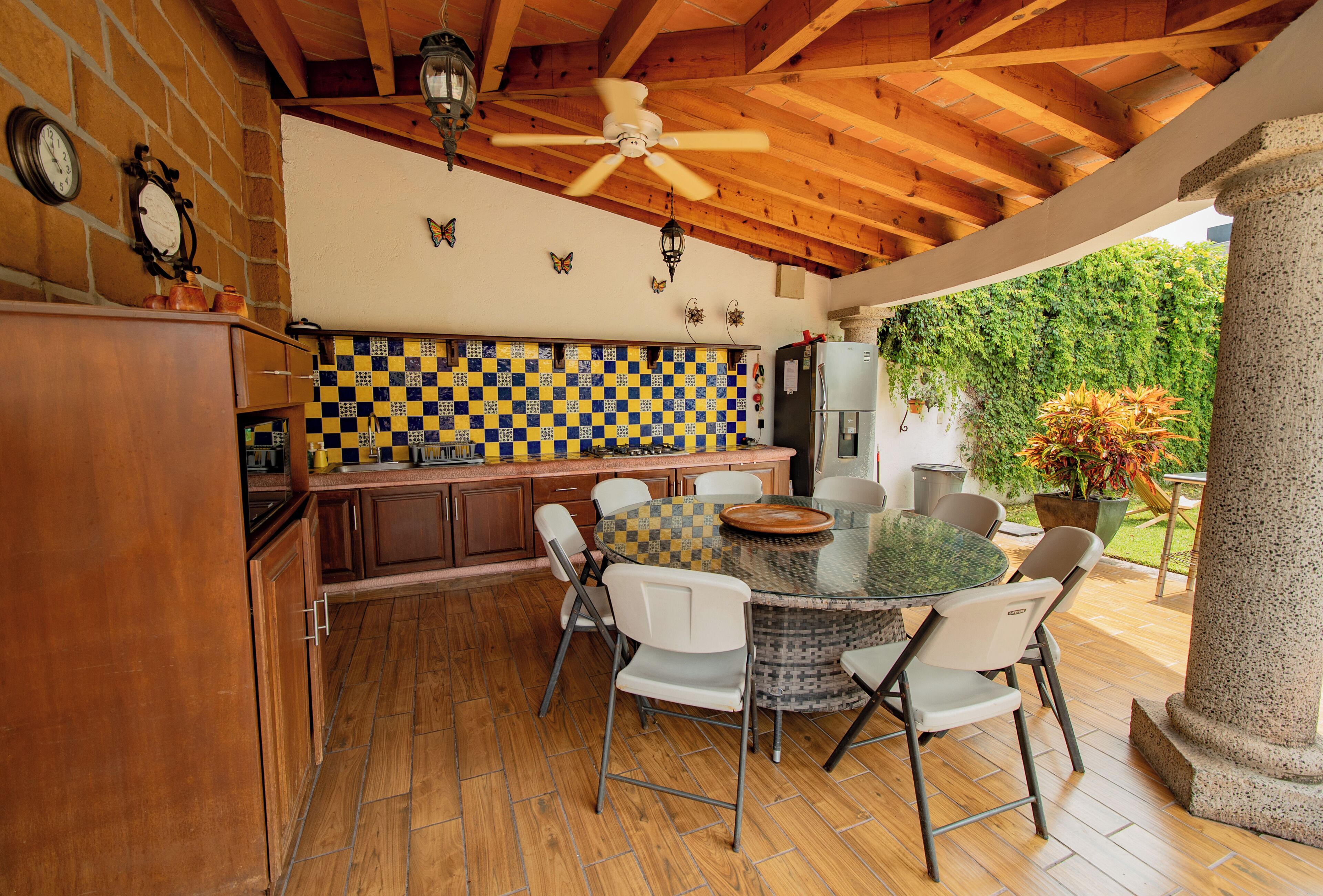 Cocina exterior con una mesa redonda y sillas, armarios de madera y un backsplash a cuadros.