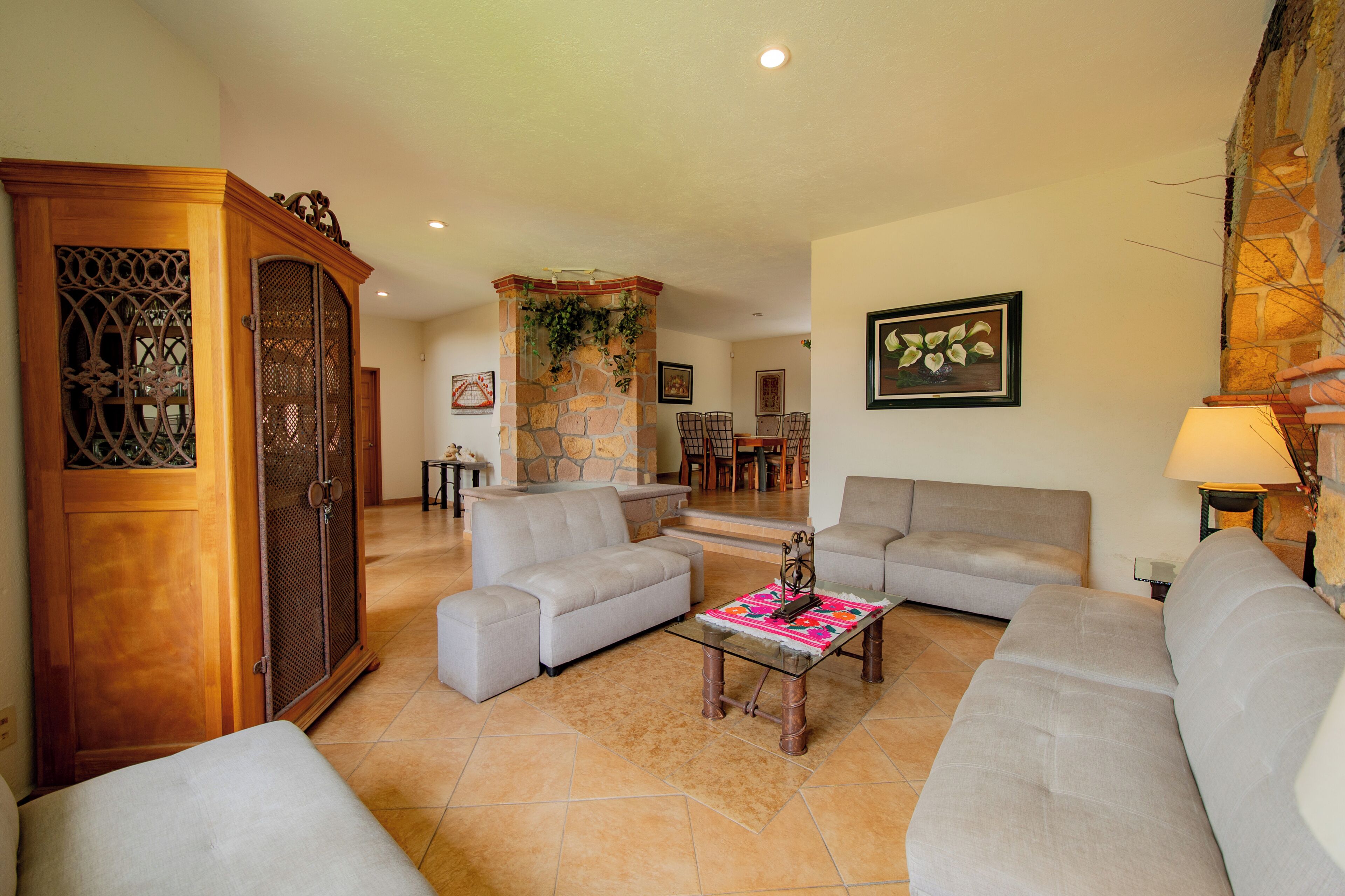A living room with a stone fireplace, a dining area, and a large wooden cabinet.