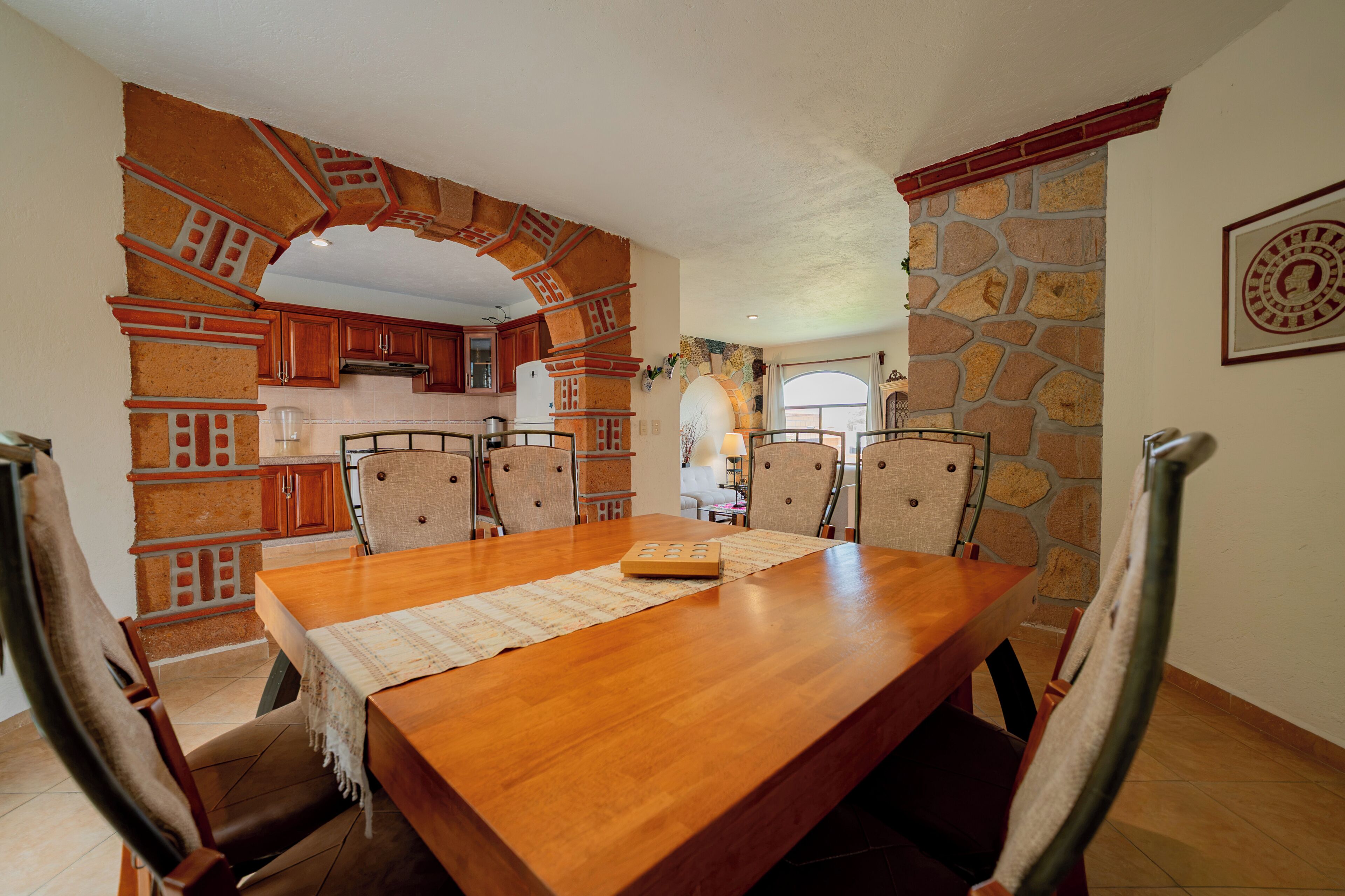 Un comedor con mesa y sillas de madera, una cocina con detalles de ladrillo y una pared de piedra.