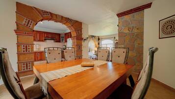 Un comedor con mesa y sillas de madera, una cocina con detalles de ladrillo y una pared de piedra.
