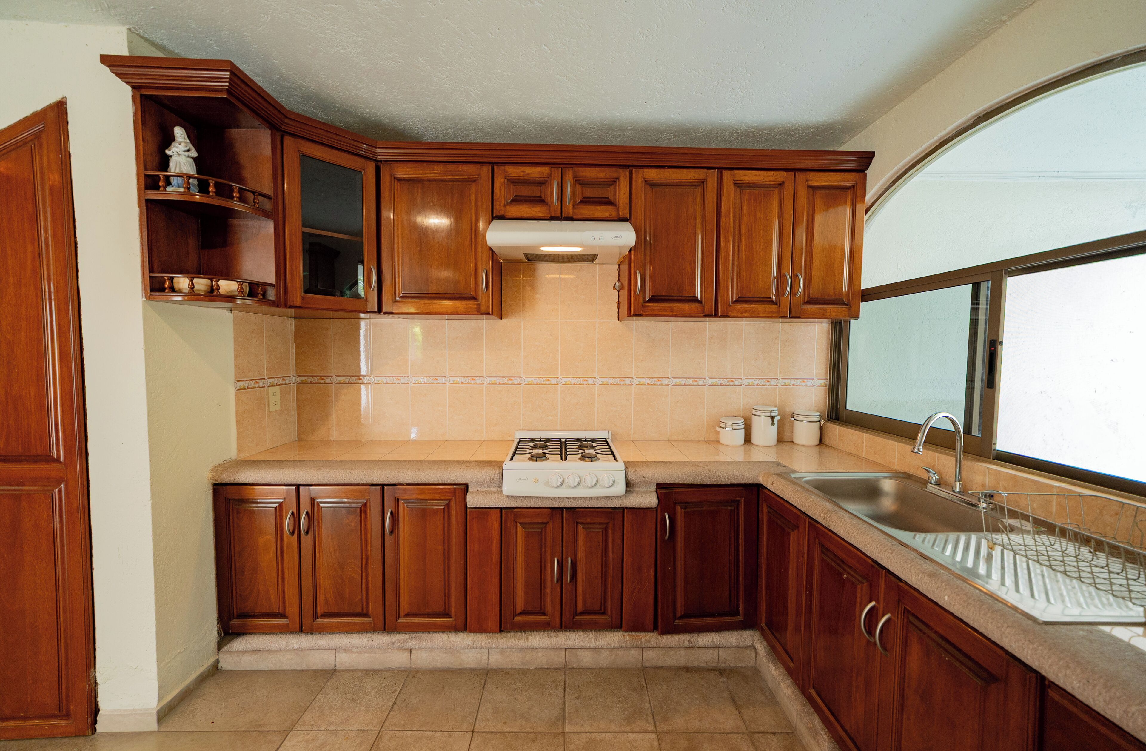 Cocina con gabinetes de madera, estufa a gas, pileta y ventana.