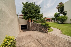 A residential area with a paved driveway leading to a stone wall, a lawn, and a pool area with lounge chairs. - Casa Melmar Pool & Garden in Cuernavaca (Tres de Mayo)
