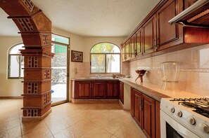 A kitchen with a brick column, wooden cabinets, a stove, and a window with a view of trees. - Casa Melmar Pool & Garden in Cuernavaca (Tres de Mayo)
