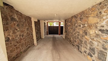 Un pasillo con paredes de piedra y piso de concreto, que conduce a una puerta con reja metálica.