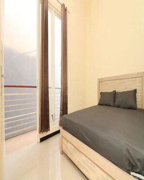 A bedroom with a bed, a window with curtains, and a view of the outside. - Cozzy Villa Cordoba (batu)