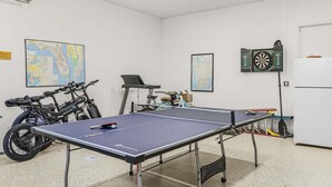 Ein Zimmer mit Tischtennisplatte, Fahrrädern, Dartscheibe und einer Karte an der Wand.