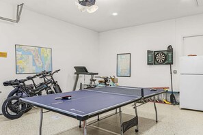 A room with a ping pong table, bicycles, a dartboard, and a map on the wall. - Relax, Paddle & Unwind in Cape Coral Paradise - Villa Cape Pearl - Roelens (Cape Coral)