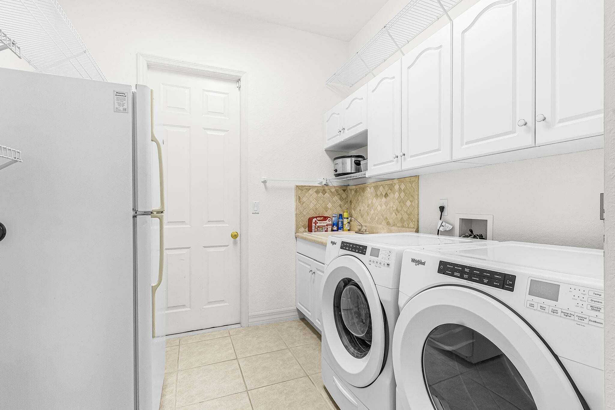 A laundry room with a white door, two front-loading washing machines, a countertop with a microwave, and cabinets above.