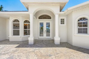 A two-story building with a symmetrical facade, featuring a central entrance with a glass door flanked by two windows, and a covered porch area. - Relax, Paddle & Unwind in Cape Coral Paradise - Villa Cape Pearl - Roelens (Cape Coral)