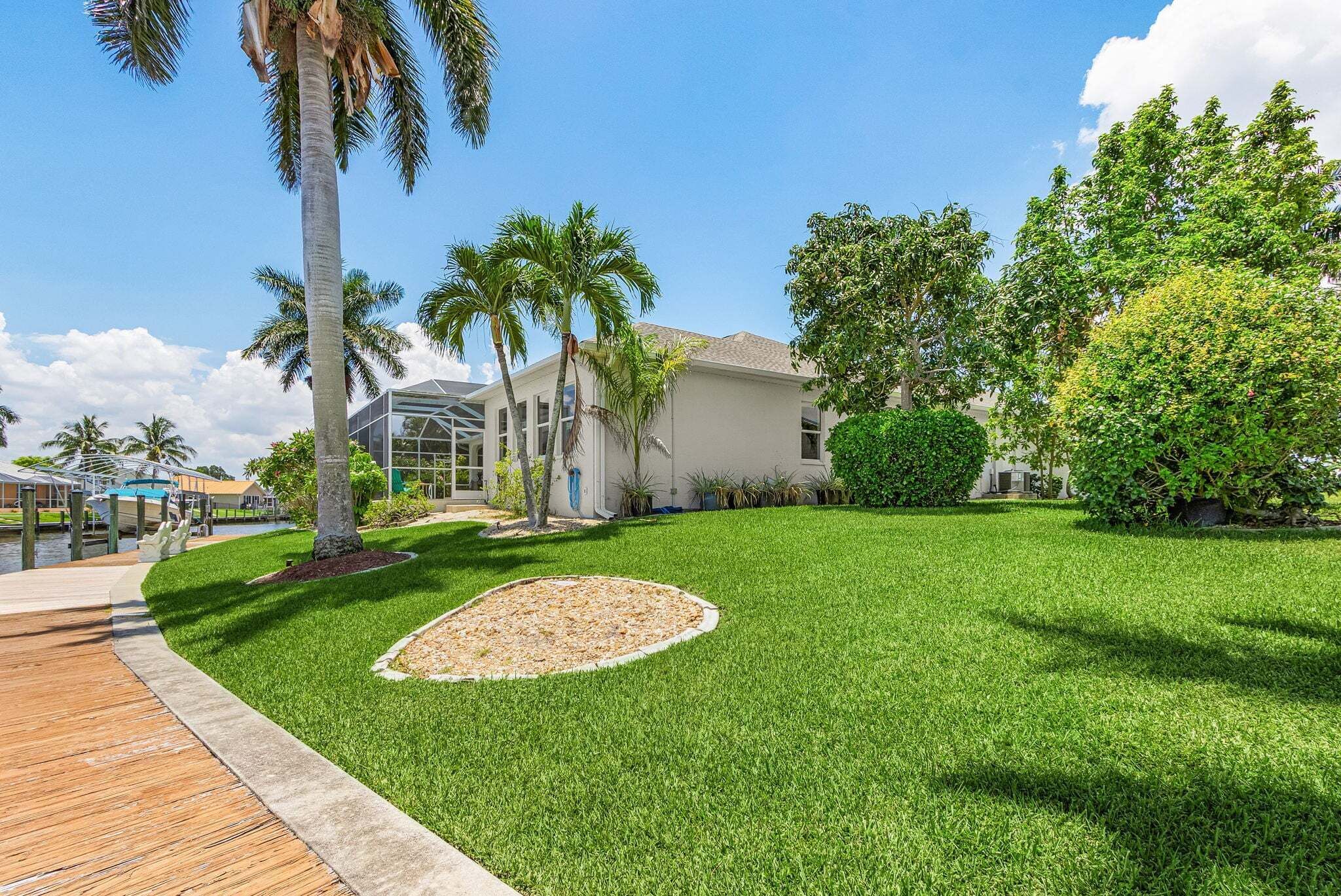 A well-maintained lawn with a circular flower bed, palm trees, and a building with large windows.