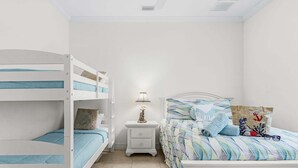 Ein Schlafzimmer mit Etagenbetten, einem Nachttisch mit Lampe, einem Bett mit gemustertem Bettbezug und einem Beistelltisch.