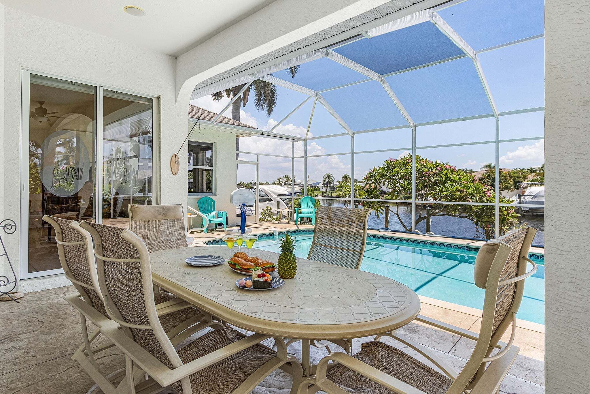An outdoor dining area with a glass-enclosed pool, wicker chairs, and a table set with food and drinks.