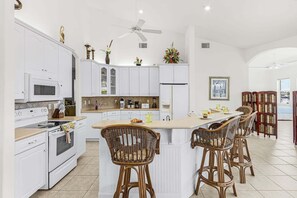 A modern kitchen with white cabinetry, a central island with bar stools, and a ceiling fan. - Relax, Paddle & Unwind in Cape Coral Paradise - Villa Cape Pearl - Roelens (Cape Coral)