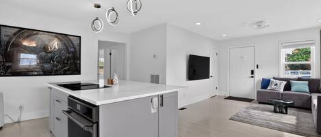 A modern kitchen with a central island, built-in oven, and a large flat-screen TV mounted on the wall.