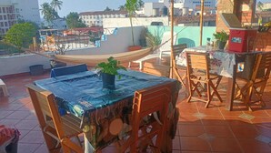 A rooftop terrace with a table and chairs, a hammock, and a view of surrounding buildings. - HOSTAL PUNTACANA (Puerto Vallarta)