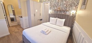 Un lit bien fait, avec une couette blanche et des oreillers, une table de chevet avec une lampe et une armoire avec un miroir.