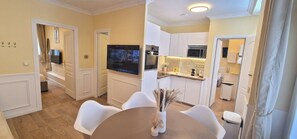 A modern kitchen with white cabinets, a flat-screen TV, and a dining area with white chairs and a vase. - Apartment - 60 sqm - Montmartre - 6p (Paris)