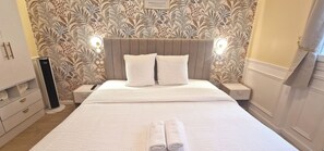 A neatly made bed with a headboard, two bedside tables with lamps, and a wall with a floral pattern. - Apartment - 60 sqm - Montmartre - 6p (Paris)