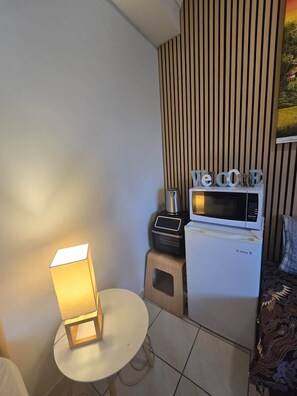 Ein kompakter Wohnbereich mit Mikrowelle, einem kleinen Tisch mit Lampe und einer Couch.