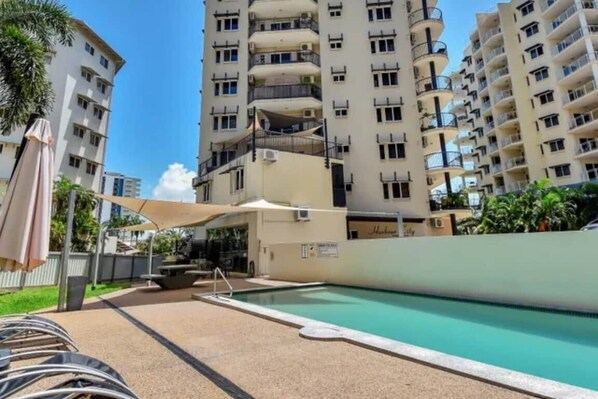 A swimming pool area with a lounge chair, a covered seating area, and a tall residential building in the background. - City Room Minutes Walk to Waterfront & CDU Campus (Darwin City)