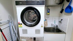 Una lavanderia piccola e funzionale con lavatrice e asciugatrice a carica frontale, un lavandino e uno straccio.