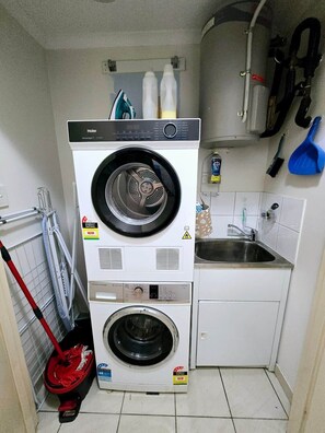 Ein kleiner Waschraum mit einer Frontlader-Waschmaschine und einem Trockner, einem Waschbecken und einem Mopp.