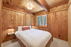 A wooden-paneled bedroom with a bed, a window, and a nightstand with a lamp. - Marigold Cabin by Tahoe Getaways - 3BR in Alpine Meadows w/ Ski Shuttle! (Alpine Meadows)
