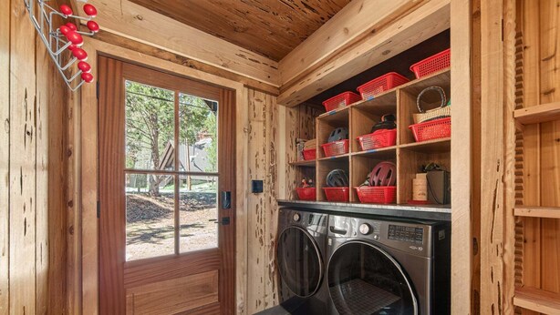 A laundry room with two front-loading washing machines, wooden shelving with red baskets, and a door with a window. - Marigold Cabin by Tahoe Getaways - 3BR in Alpine Meadows w/ Ski Shuttle! (Alpine Meadows)