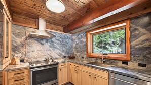 A kitchen with wooden cabinets, a stainless steel oven, a sink, and a window with a view of trees. - Marigold Cabin by Tahoe Getaways - 3BR in Alpine Meadows w/ Ski Shuttle! (Alpine Meadows)