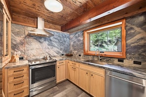 A kitchen with wooden cabinets, a stainless steel oven, a sink, and a window with a view of trees. - Marigold Cabin by Tahoe Getaways - 3BR in Alpine Meadows w/ Ski Shuttle! (Alpine Meadows)