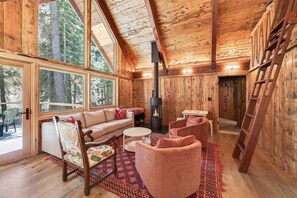 Un interior de cabaña acogedor, con un sofá, sillas, una mesa y una chimenea.