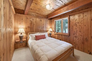 A wooden-paneled bedroom with a bed, two bedside lamps, and a window. - Marigold Cabin by Tahoe Getaways - 3BR in Alpine Meadows w/ Ski Shuttle! (Alpine Meadows)