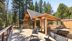 A wooden deck with outdoor furniture, a covered seating area, and a view of a forested landscape. - Marigold Cabin by Tahoe Getaways - 3BR in Alpine Meadows w/ Ski Shuttle! (Alpine Meadows)