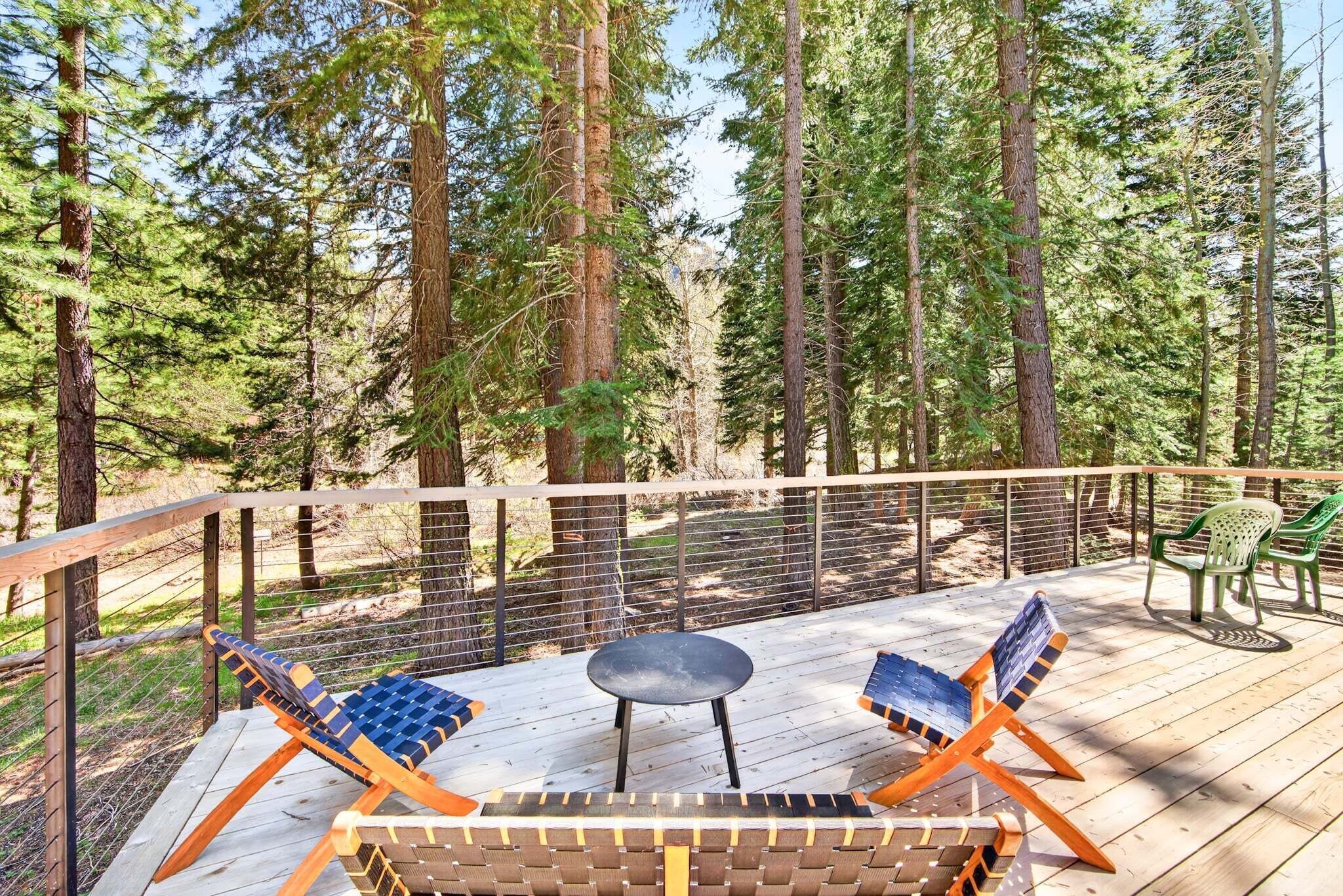 Une terrasse dotée de mobilier d’extérieur, entourée d’une balustrade en bois et bordée de grands arbres.