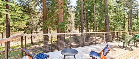 A deck with outdoor furniture, surrounded by a wooden railing and tall trees.