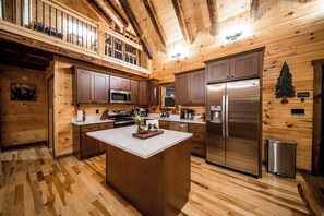 A modern kitchen with wooden walls, a central island, stainless steel appliances, and a balcony with railings. - Brand New Cabin | Theater | Game Room | Hot Tub (Logan)