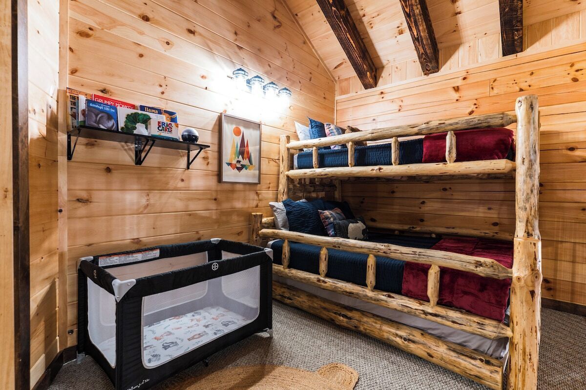 Un cuarto de madera acogedor con literas, un corral para bebés y una estantería con artículos infantiles.