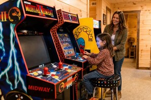 Ein Kind spielt ein Videospiel an einer Midway Arcade-Maschine in einem Raum mit Holzwänden.