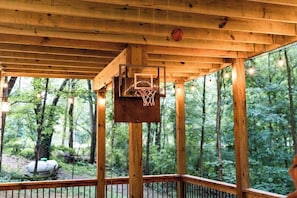 A basketball hoop on a wooden deck with a forest backdrop. - Brand New Cabin | Theater | Game Room | Hot Tub (Logan)