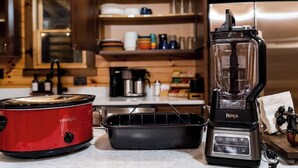 Et køkken med en rød slowcooker, en sort Ninja blender og en sort bageplade.