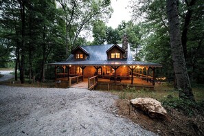 Eine Holzhütte mit Veranda, Holzgeländern und einem Steinsschornstein.