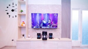 A modern living room with a mounted TV, a white entertainment unit, and a clock on the wall. - Cozzy Villa Zast (malang)