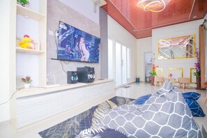 A modern living room with a flat-screen TV mounted on the wall, a sofa with patterned cushions, and a ceiling with a unique light fixture. - Cozzy Villa Zast (malang)