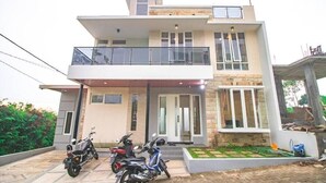 A two-story modern house with a balcony, a driveway, and two motorcycles parked outside. - Cozzy Villa Zast (malang)