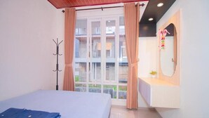 A bedroom with a bed, a coat rack, a window with curtains, and a bathroom vanity with a mirror. - Cozzy Villa Zast (malang)