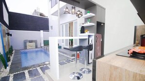 A modern kitchen with a bar area, a pool, and a staircase leading to an upper level. - Cozzy Villa Zast (malang)